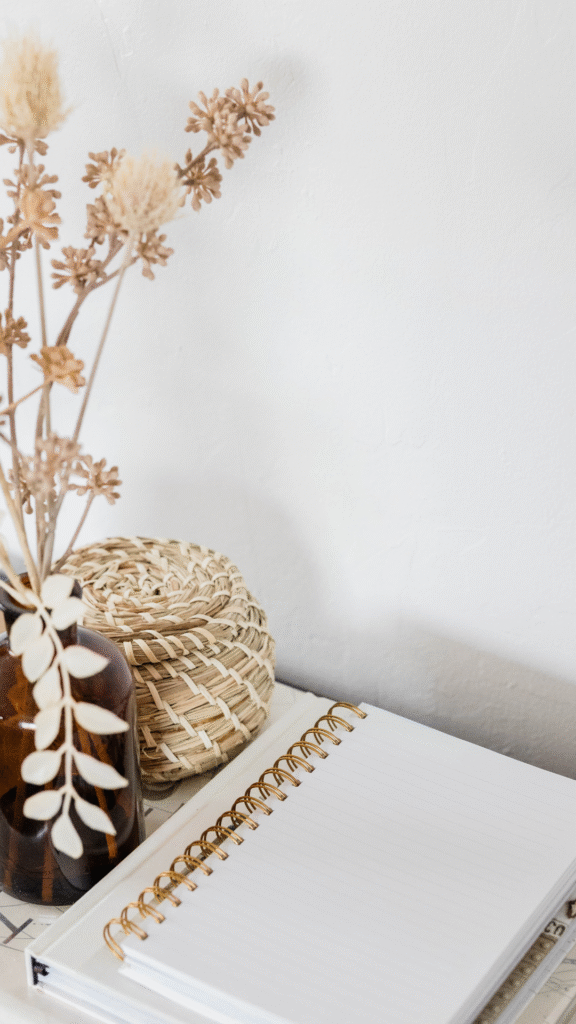 fleurs séchées dans un vase teint, corbeille en osier et carnet vierge ouvert sur un bureau